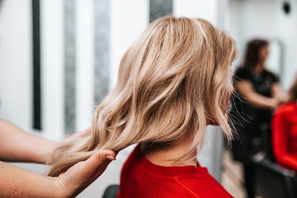 Gros plan d’une tresse latérale complexe réalisée sur des cheveux blonds avec reflets dorés et cuivrés, tandis que la coiffeuse ajuste les mèches dans un environnement professionnel de salon – Euphoria Hair & Beauty Studio.