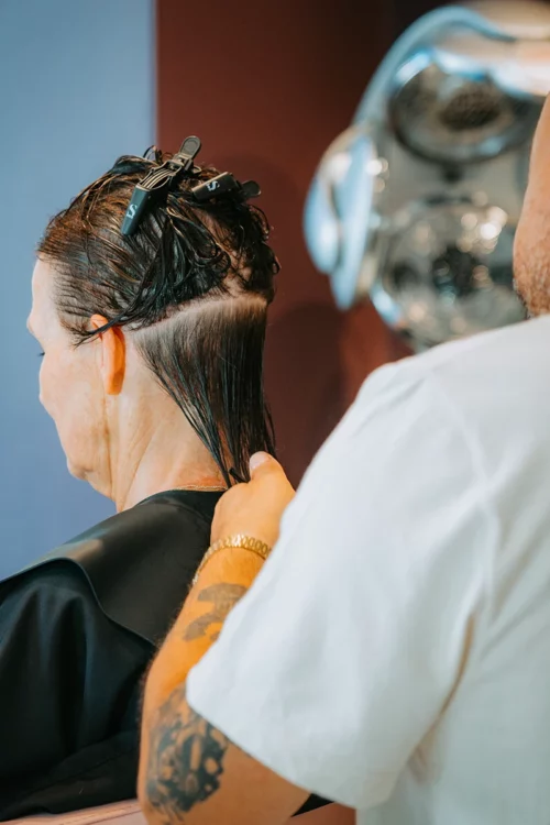 Coiffeur travaillant une section de cheveux mouillés avec pinces, préparation de la coupe en salon.