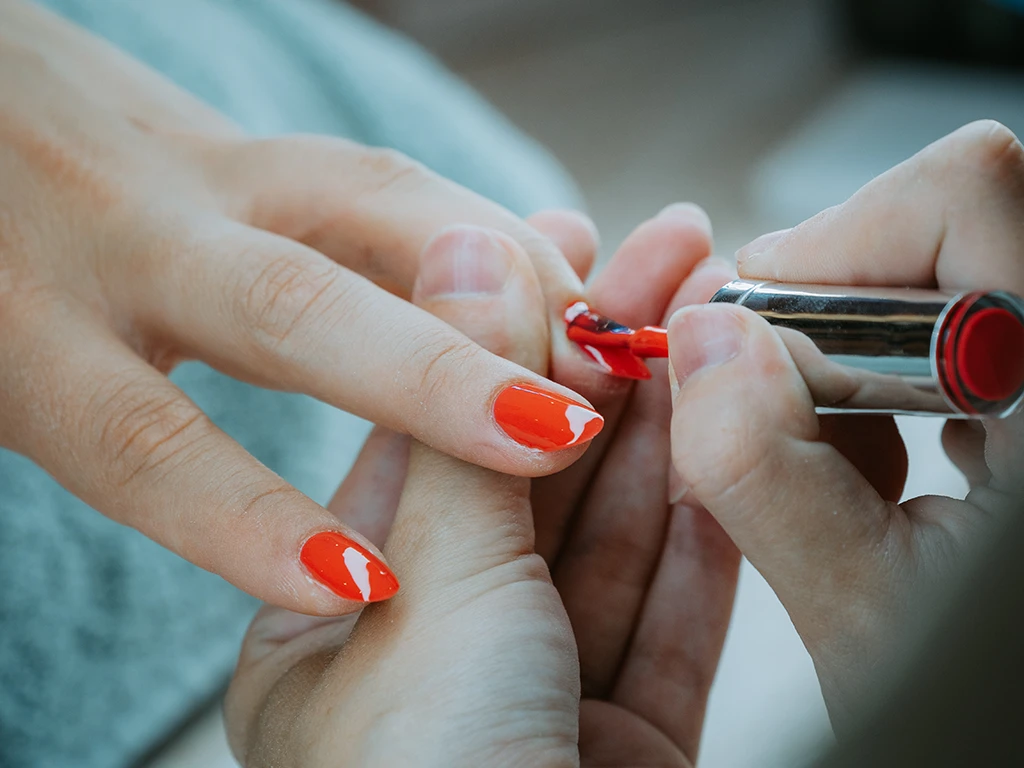 Application de vernis rouge lors d’une manucure professionnelle, gros plan des mains.