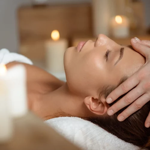 Massage du visage relaxant dans une cabine éclairée aux bougies, femme allongée, ambiance spa.